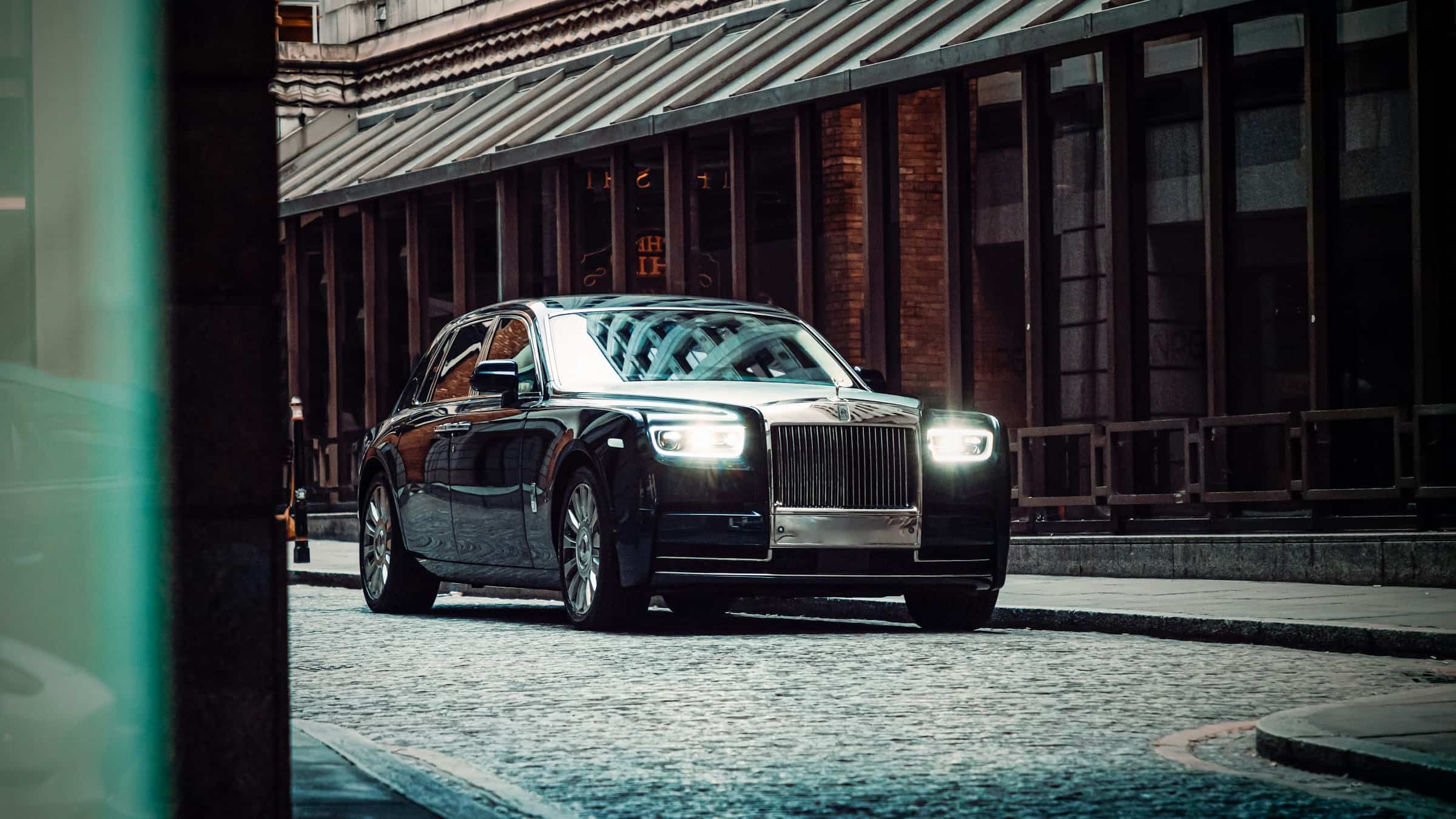 A black Rolls-Royce Phantom waiting on a quiet, lamplit London street at night